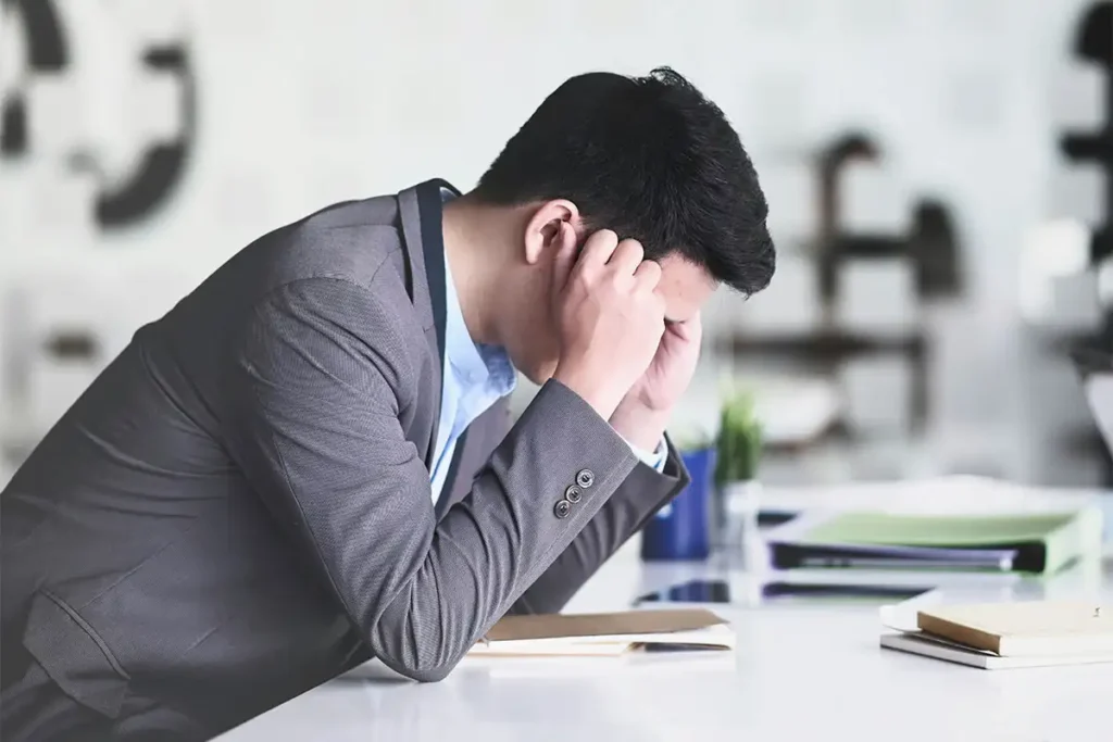 A man in a suit sits at a desk, his head in his hands, reflecting the struggle of managing depression at work