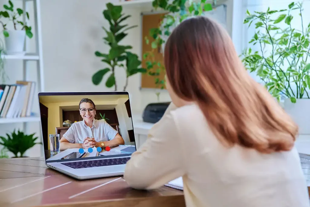 A woman seated at a desk, using a laptop for virtual mental health therapy
