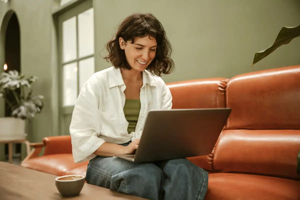 A woman comfortably sitting on a couch, engaged with her laptop, illustrating a blend of relaxation and productivity
